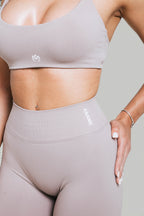 A N A M E Mocha Cappuccino sports bra with logo detail worn by a model, featuring a supportive fit for workouts.