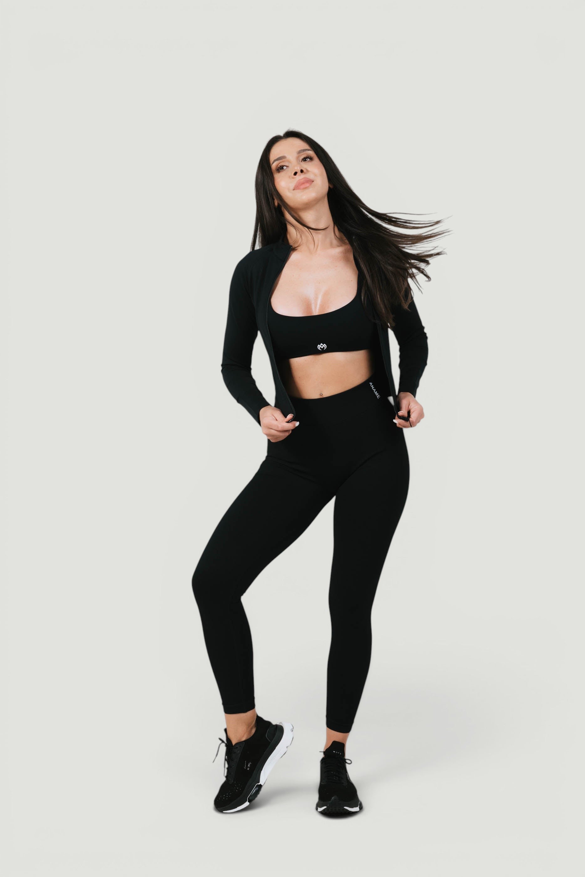 A N A M E Core Jacket in black worn by a model with matching leggings and sports bra for a versatile athletic look.