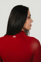 A N A M E Core Jacket in red wine, featuring a high neck and minimalist logo on the back, worn by a woman.