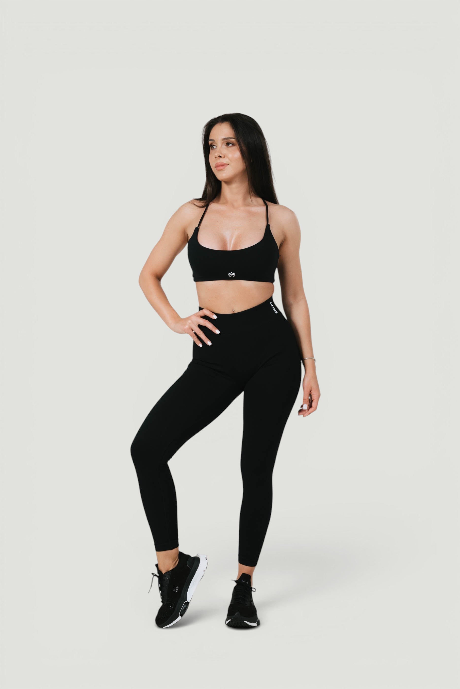 A N A M E black midnightTwisted-back Bra worn by a model with matching leggings and sneakers for a workout look.