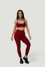 A N A M E Twisted-back Bra in deep red wine worn by a model with matching high-waisted leggings for a workout set.