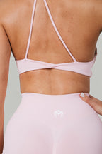 A N A M E pink rose sports bra with delicate straps and a twisted-back detail worn by a woman.