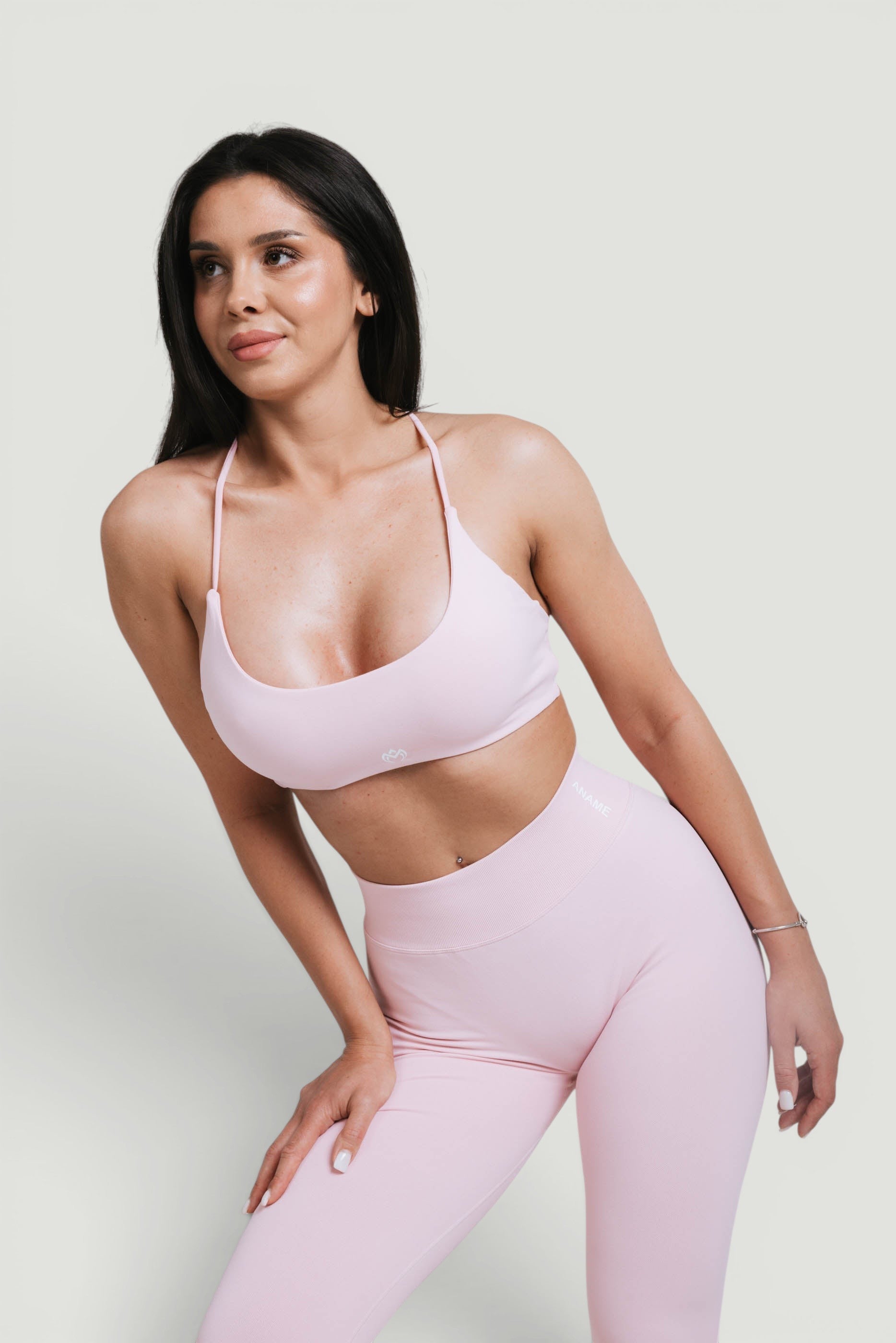 A N A M E pink rose sports bra with delicate straps and a twisted-back design worn by a model in a studio.