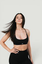 A N A M E black midnight sports bra with delicate straps and a feminine design worn by a model against a neutral background.